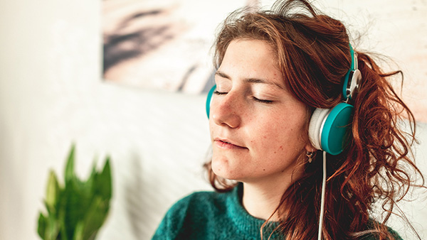 Jonge vrouw draagt blauwe hoofdtelefoon en luistert naar muziek met gesloten ogen.