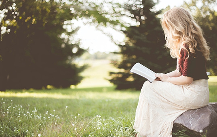 Vrouw met blond haar leest boek in tuin