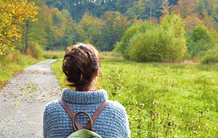 jonge vrouw draagt blauwe trui en bruin rugzakje tijdens wandeling