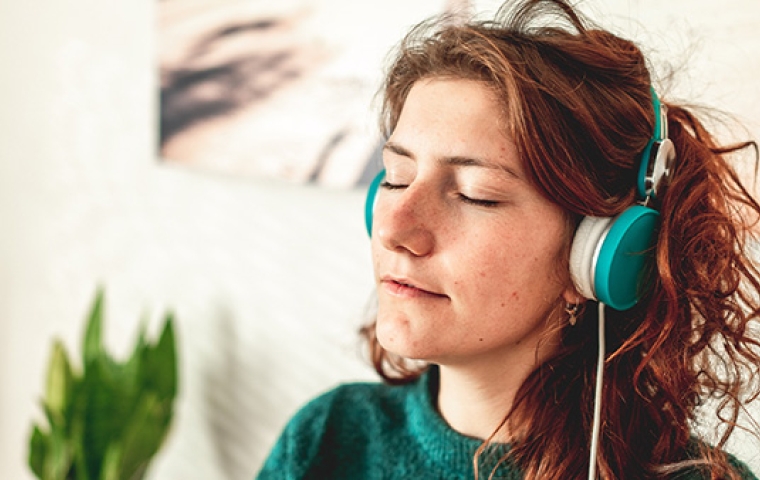 Jonge vrouw draagt blauwe hoofdtelefoon en luistert naar muziek met gesloten ogen