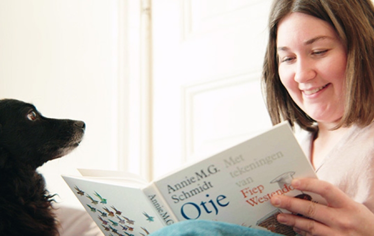 Jonge vrouw met kort haar lees in een boek en haar zwarte hond  zit ernaast